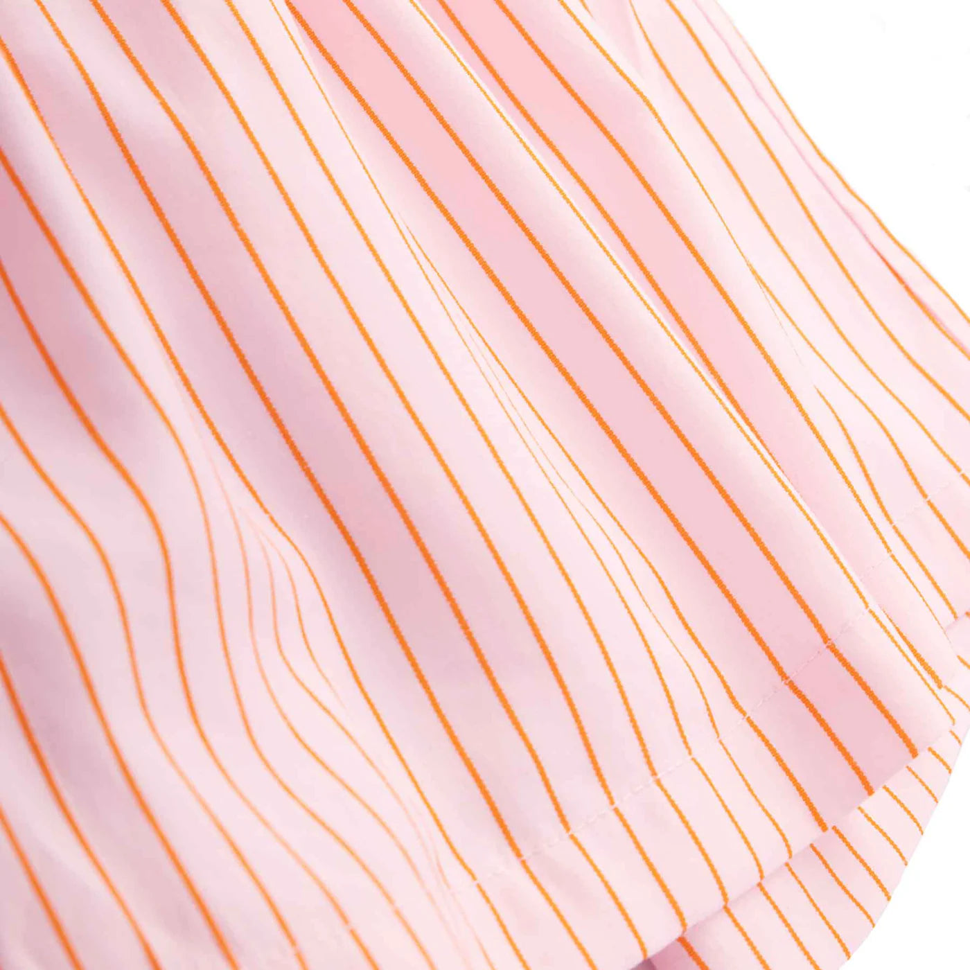 A close-up of a pink fabric with thin vertical orange stripes, similar to Cherry Gingham. The soft and light texture with gentle folds resembles the style of Mama Everyday Shorts Sunset Stripe by LITTLE THE LABEL, ideal for daily wear.