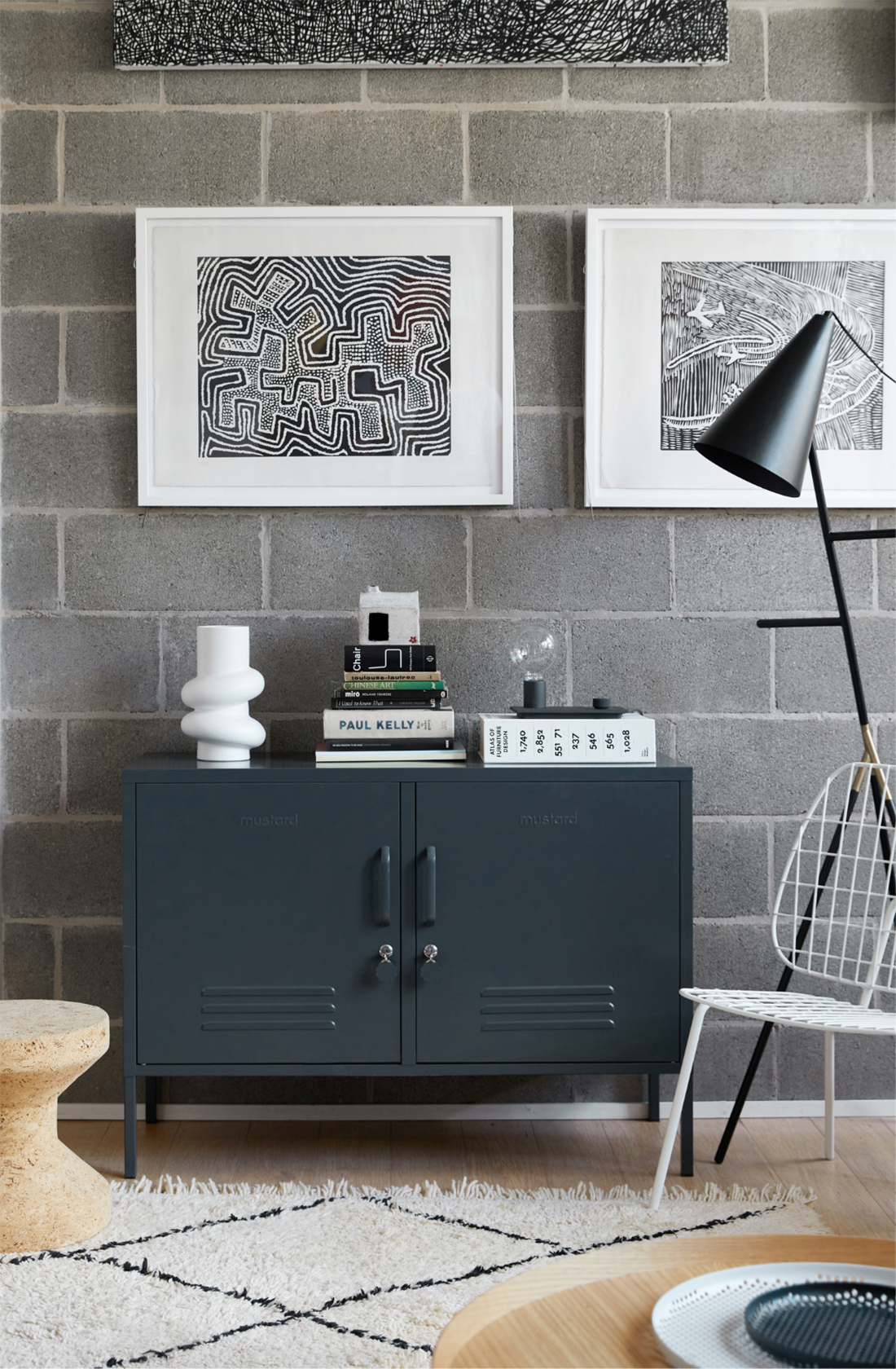 The lowdown locker in slate against a grey brick wall with books and a vase on top..