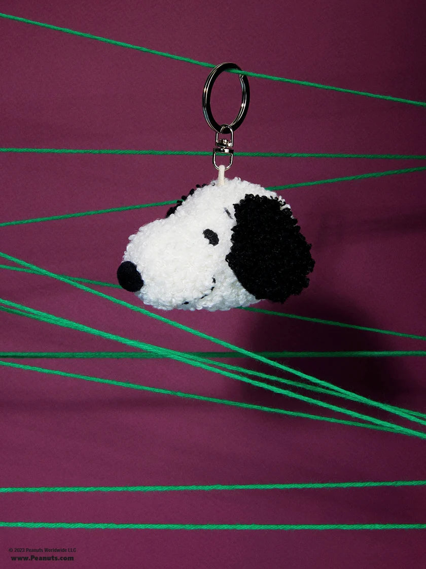 The Bon Ton Toys - Snoopy ECO Tiny Teddy Cream Keychain 4.5cm by BON TON TOYS X MIFFY, made from recycled polyester, hangs from green strings against a purple background.