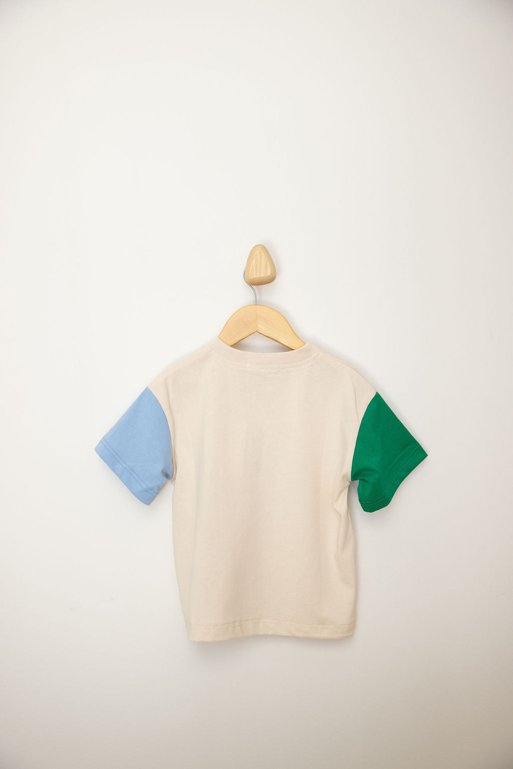 The Sunday Records Tee Blue/Green by SUNDAY SIBLINGS presents an oversized fit, displayed on a wooden hanger against a white backdrop. The cream-colored child's T-shirt showcases one sleeve in light blue and the other in green, providing an ideal mix of style and comfort.