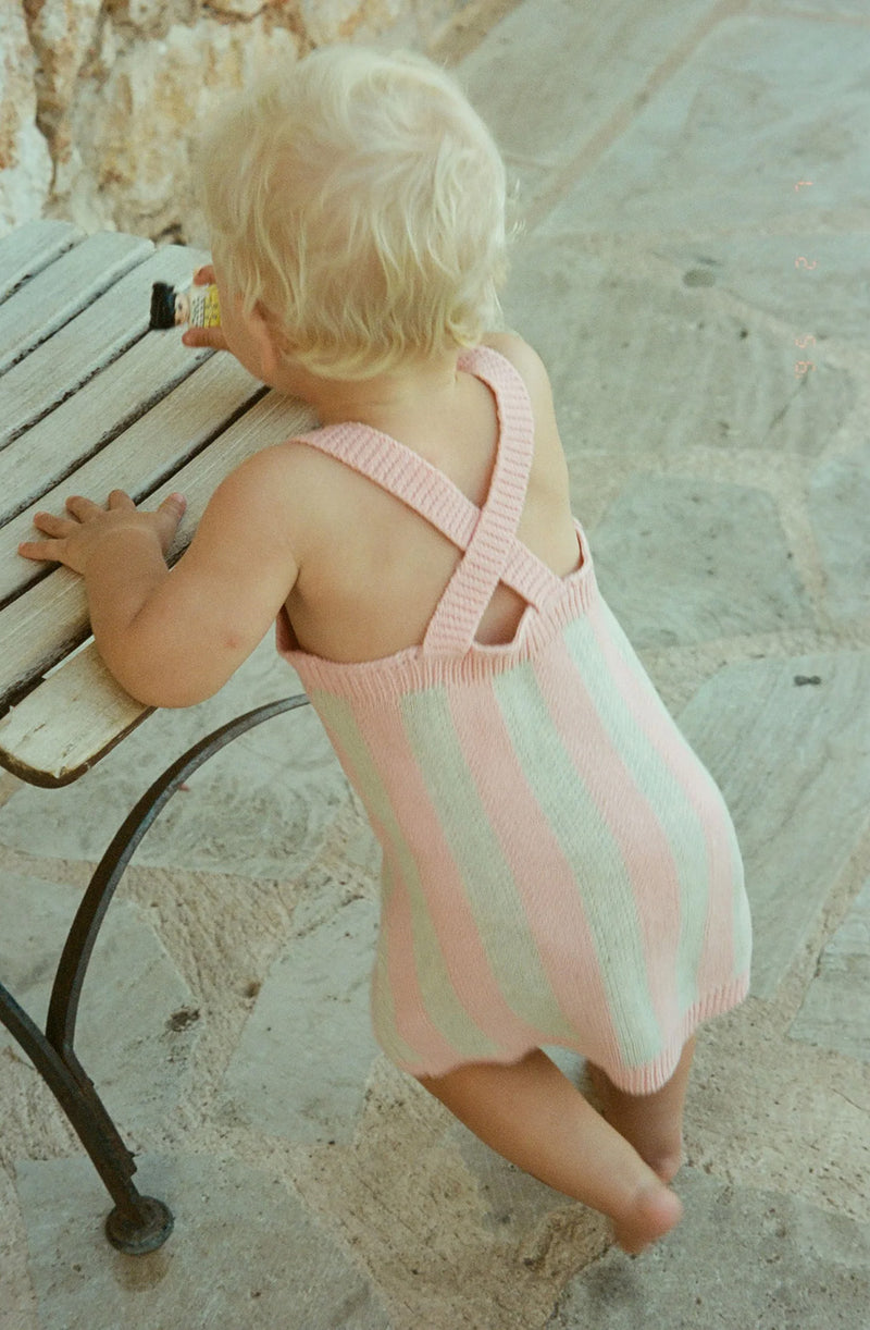 Baby standing holding onto a chair wearing the rosa knit dress