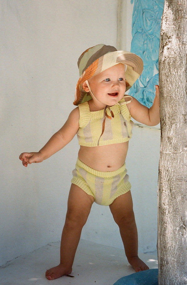 Baby holding onto tree trunk wearing the limon knit set with a bucket hat