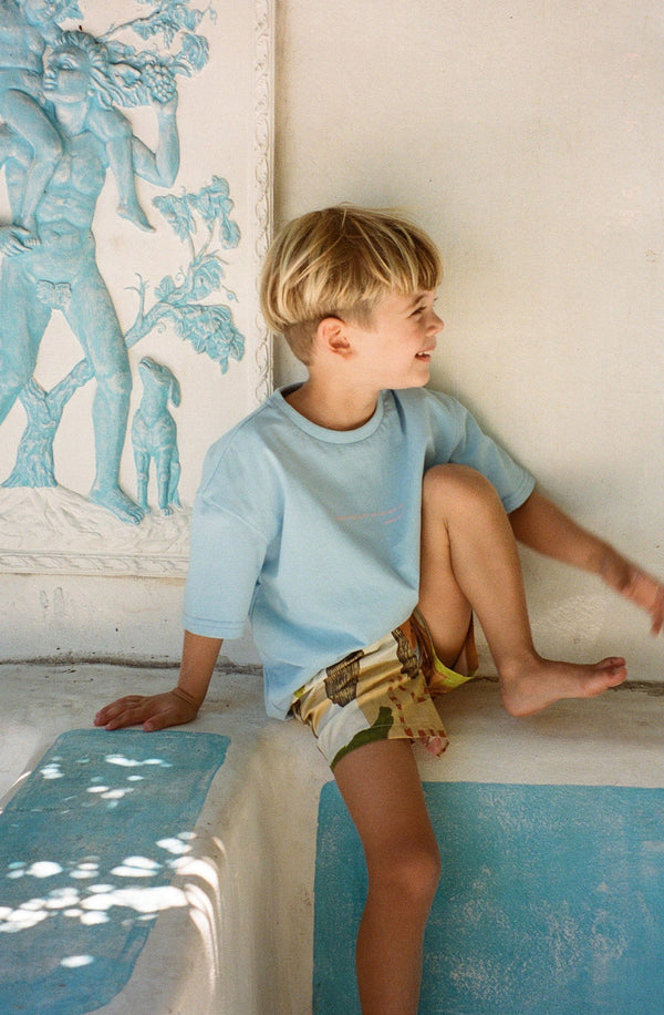 Boy sitting on wall wearing the sun and sea tee with printed shorts
