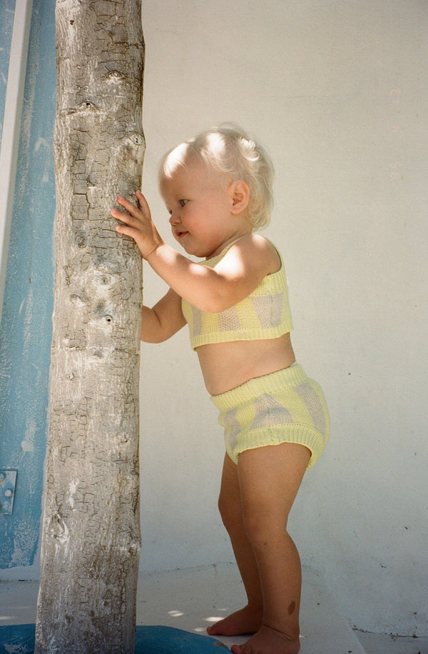 Side view of baby wearing the limon knit set holding onto a tree trunk