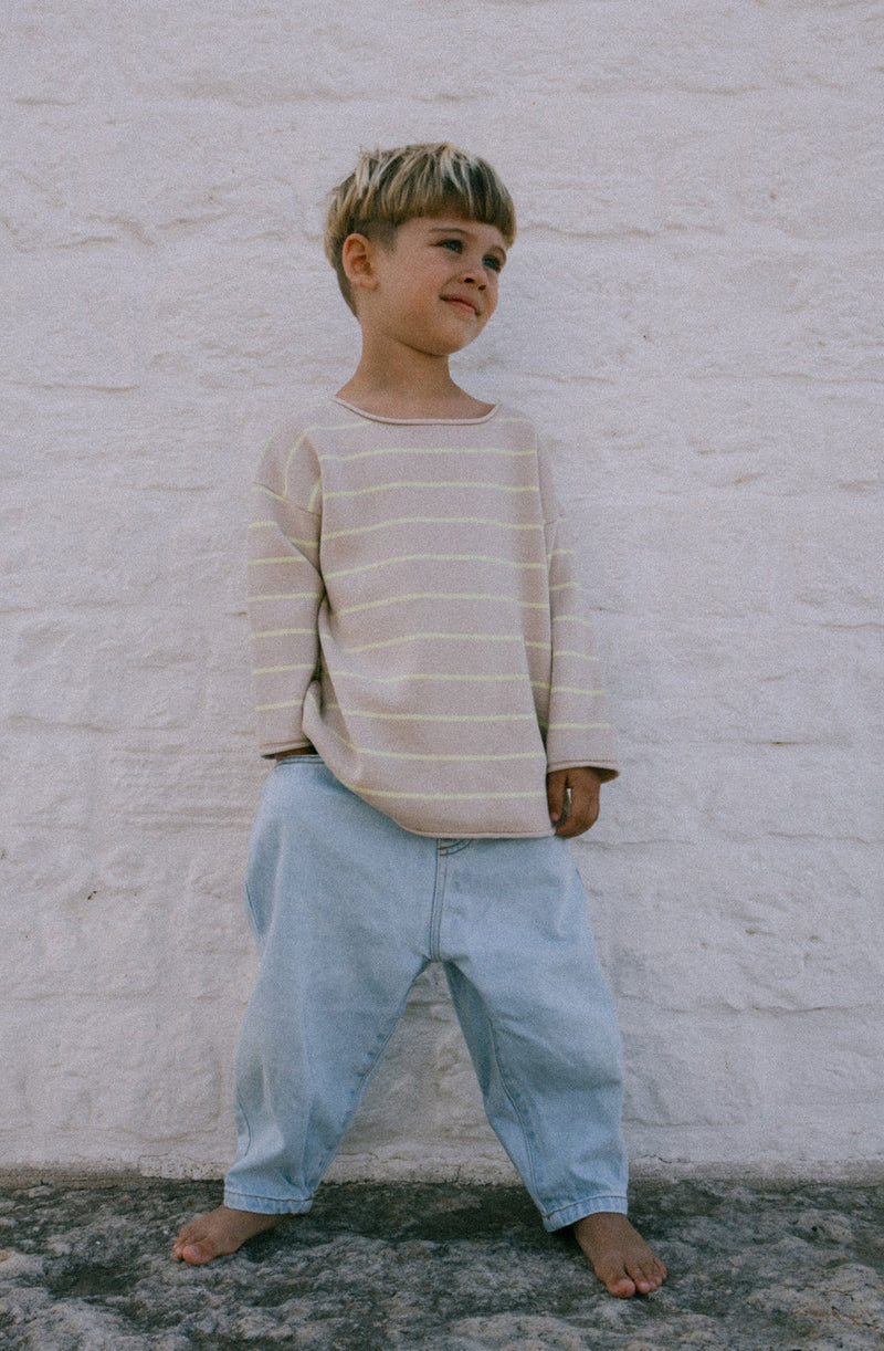 Boy wearing the citrus stripe knit with jeans standing against a white brick wall