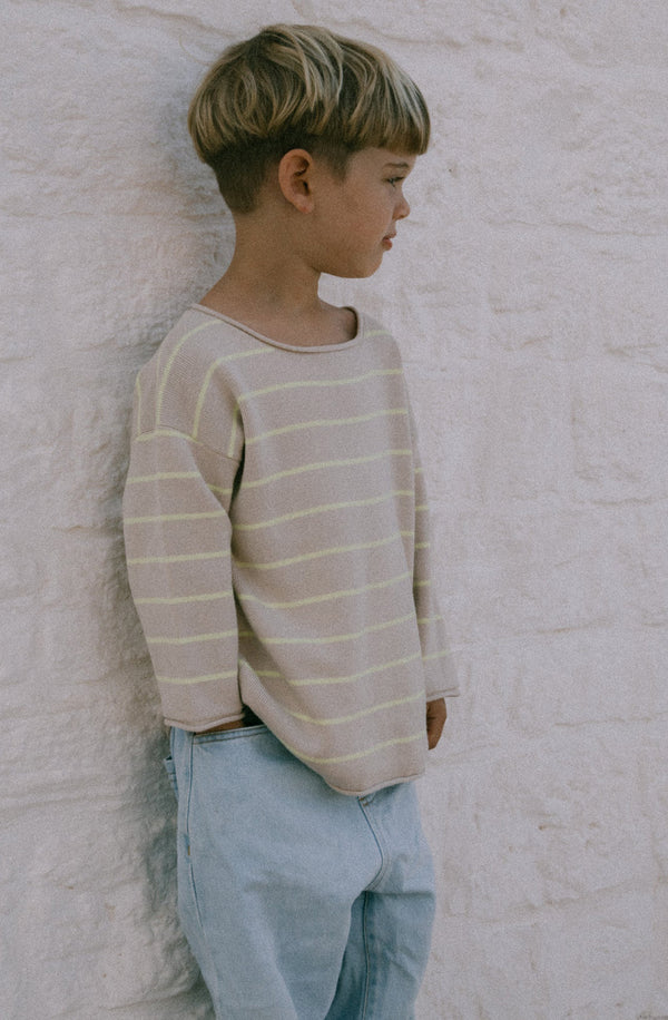 Boy standing on the side wearing the citrus striped knit with light blue jeans 