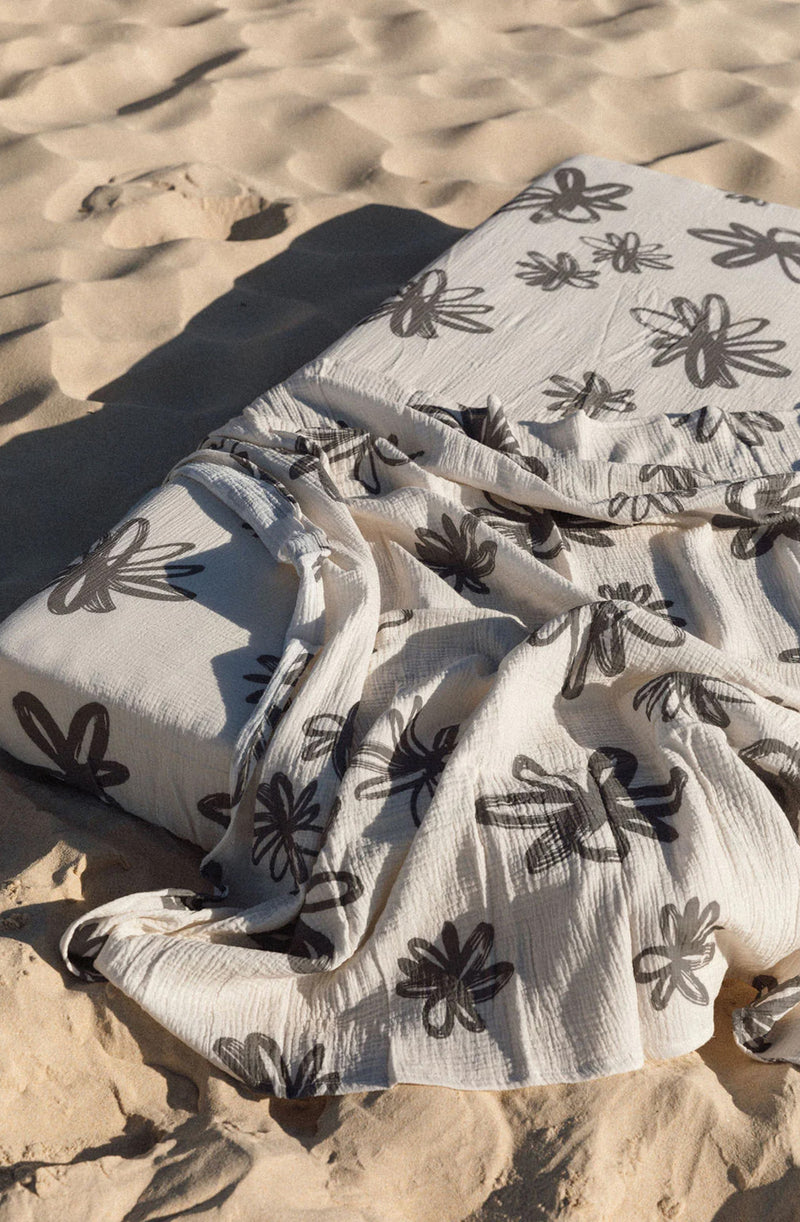 Flora swaddle laid over cot mattress in the sand at the beach