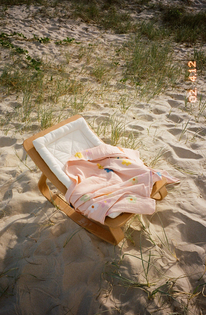 Bloom swaddle laid out on timber baby rocker at the beach