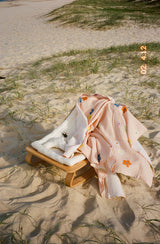 Bloom swaddle draped over timber baby rocker at the beach
