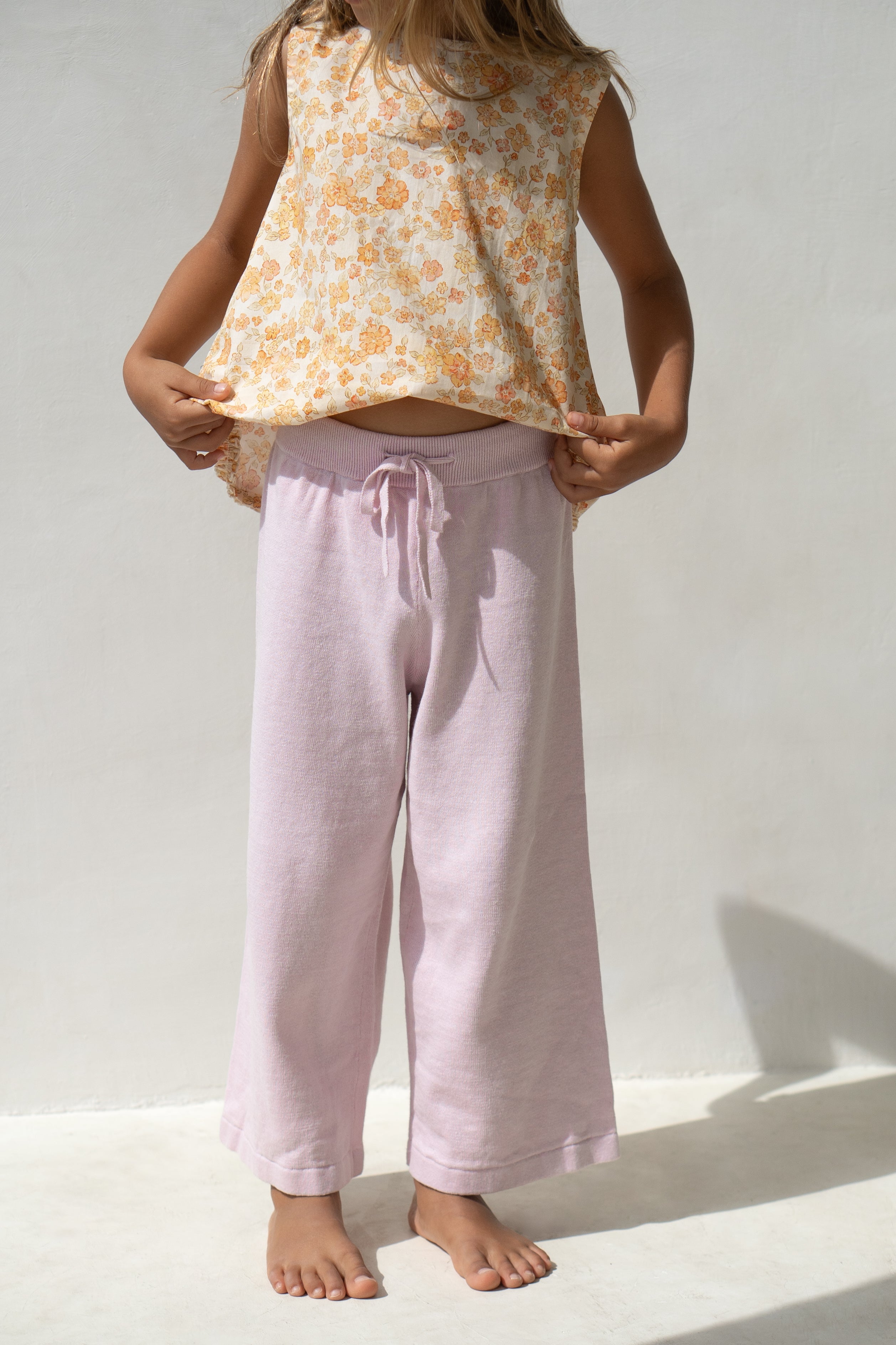 A young girl wearing the tilly blouse in buttercup with purple pants.