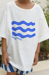 Boy wearing oversized white t-shirt with blue wave print and blue/white stripe shorts