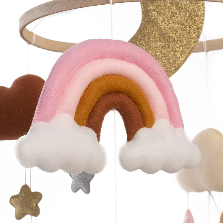 The ROOMI & ME Roomi & Me - Baby Mobile Sparkly Galaxy is a handmade felt mobile with a pink and brown rainbow, white clouds, golden moon, brown cloud, and stars—ideal for gentle visual stimulation in your nursery.