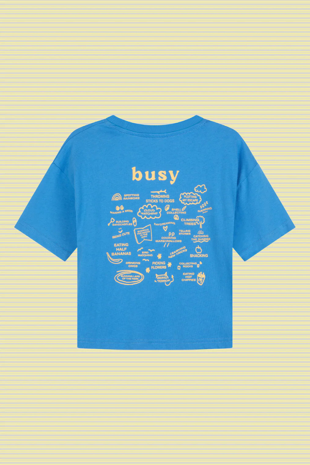 The Lenn Label - Busy Tee Sunny by LENN LABEL is a blue kids' cotton jersey tee featuring "busy" at the top and white doodles on the back. It has an oversized fit for comfort and is shown against a yellow striped background.