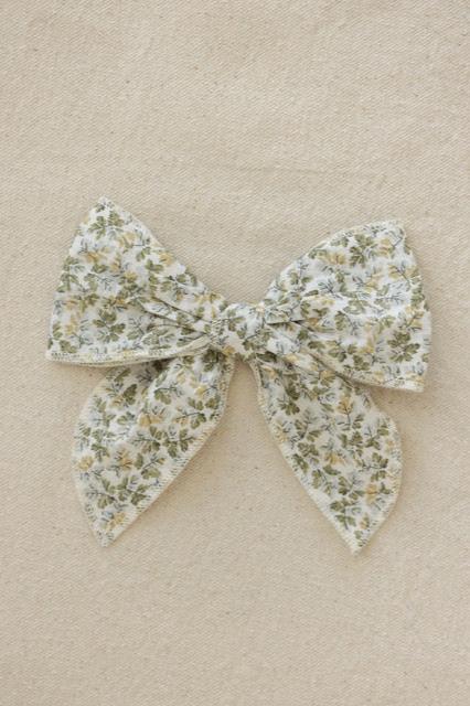 The Cotton Bow Coorabell, a delightful handmade fabric hair bow from VALENCIA BYRON BAY, featuring a floral pattern in shades of green and beige, is displayed against a light, textured background. This charming hair accessory boasts two large loops and two trailing ends.