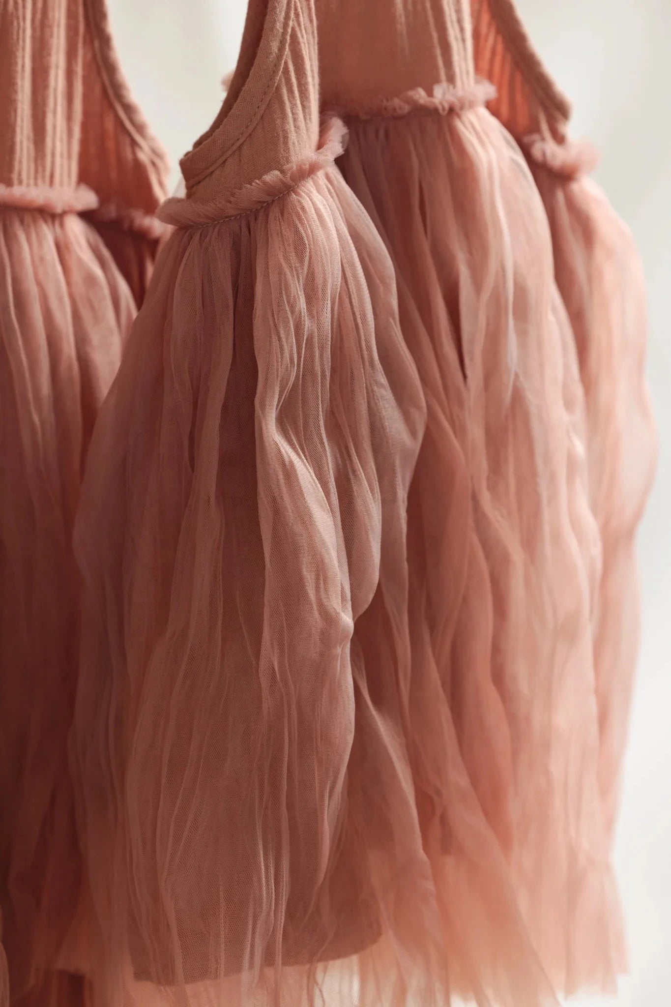 Close-up of delicate hangings of the Bangalow Tutu Dress in Antique Rose by VALENCIA BYRON BAY. The soft, flowing fabric, reminiscent of a party dress, captures the essence of light pink tulle skirts. The image focuses on the texture and details of the gauzy material, exuding a sense of lightness and grace. These skirts evoke the charm and elegance inherent in every Bangalow Tutu.