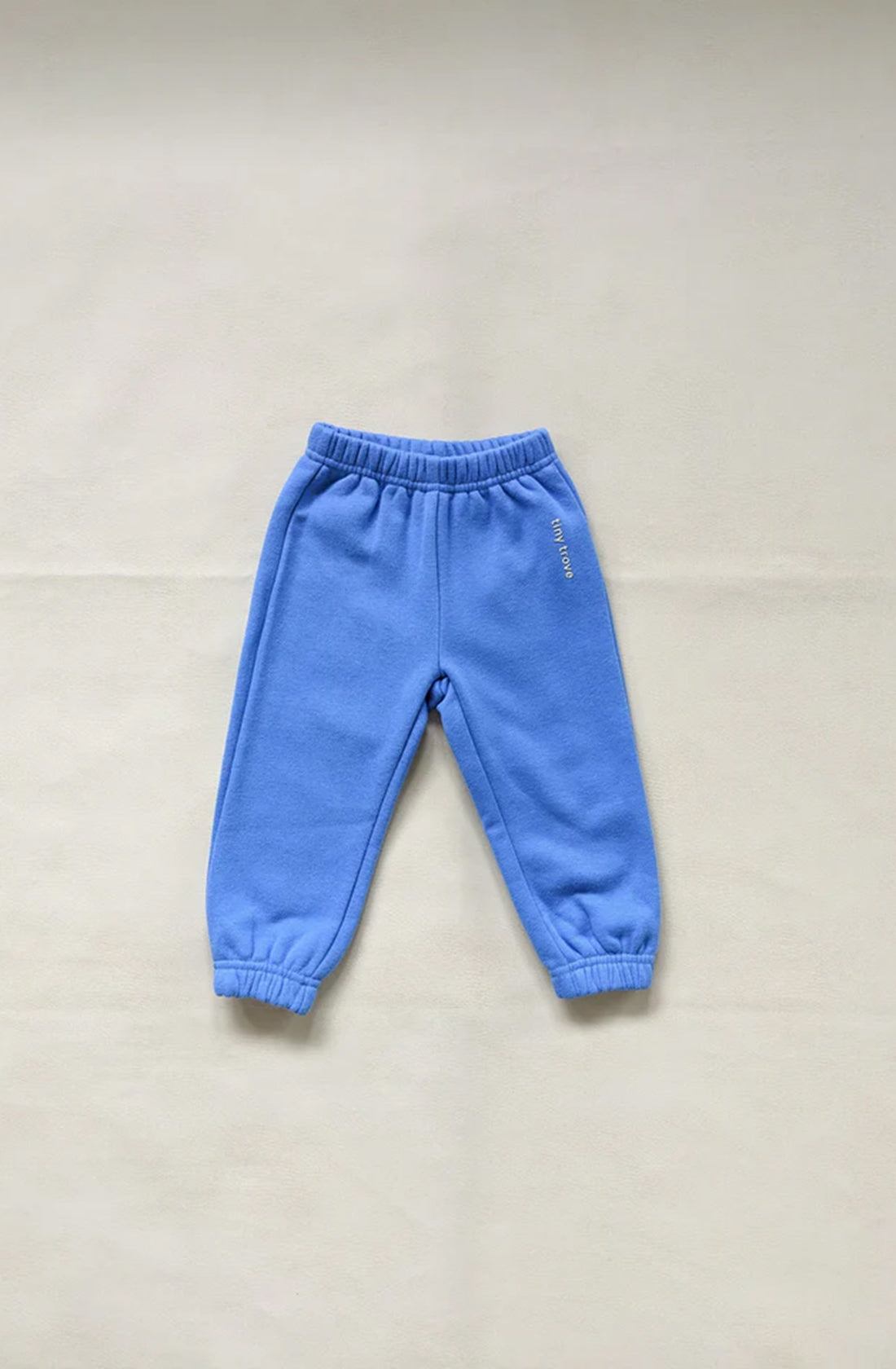 A pair of Woodie 3D Logo Tracksuit Ocean children's sweatpants from TINY TROVE is laid out on a flat surface. The fleece cotton sweatpants feature an elastic waistband and cuffs, with fabric that appears soft and cozy, ideal for comfortable wear.