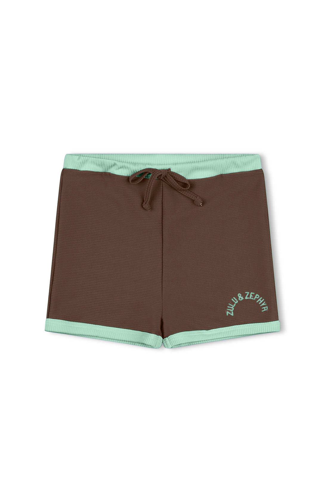 The Mini Rib Surf Short Cacao by ZULU & ZEPHYR features brown shorts with a light green waistband and leg cuffs, along with a drawstring at the waist. The brand's name, "ZULU & ZEPHYR," is written in light green lettering on the bottom left leg. Made from ECO MADE Recycled Spandex, these shorts offer a simple yet sporty design.