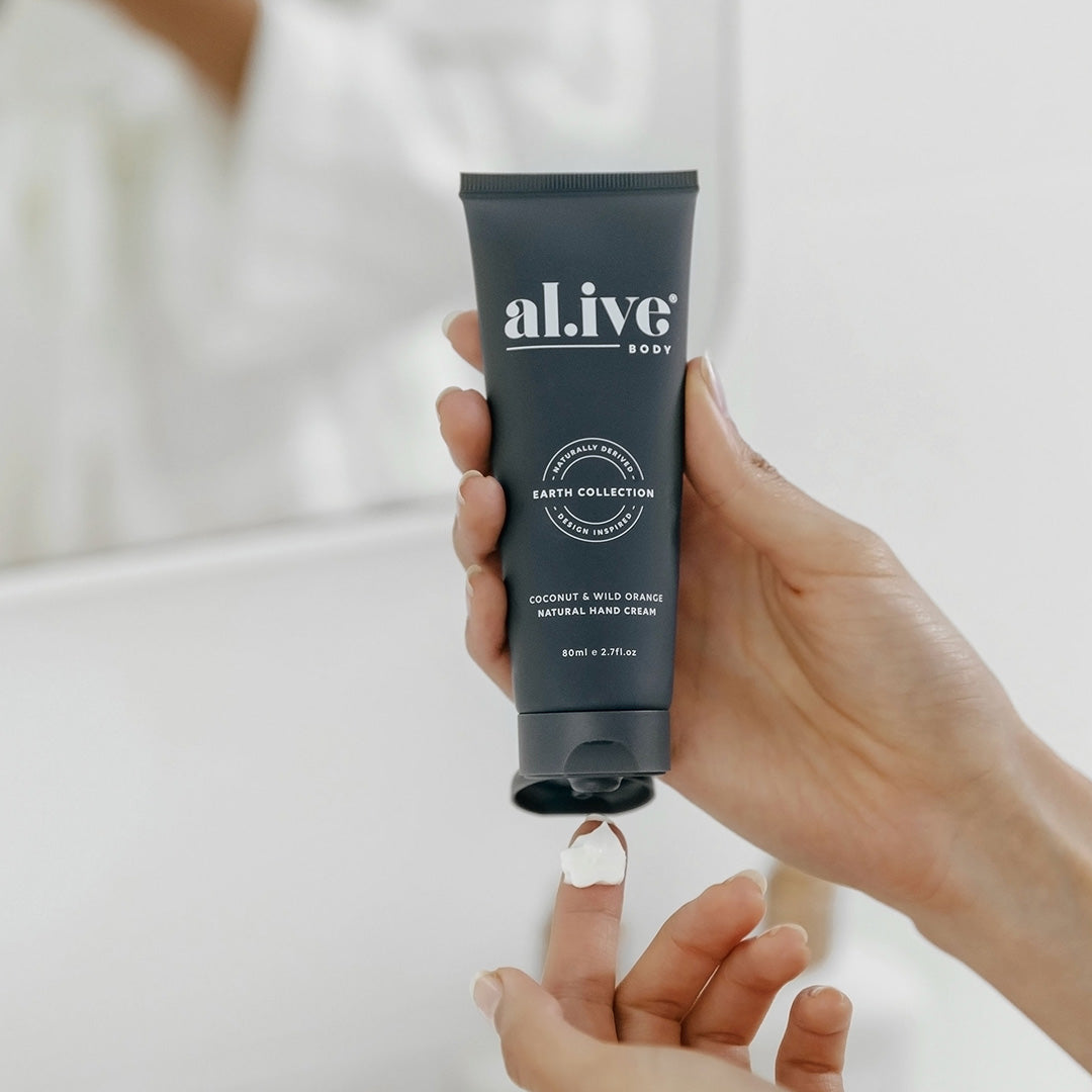 A women squeezing white hand cream from a tube of coconut and wild orange natural hand cream by al.ive body.