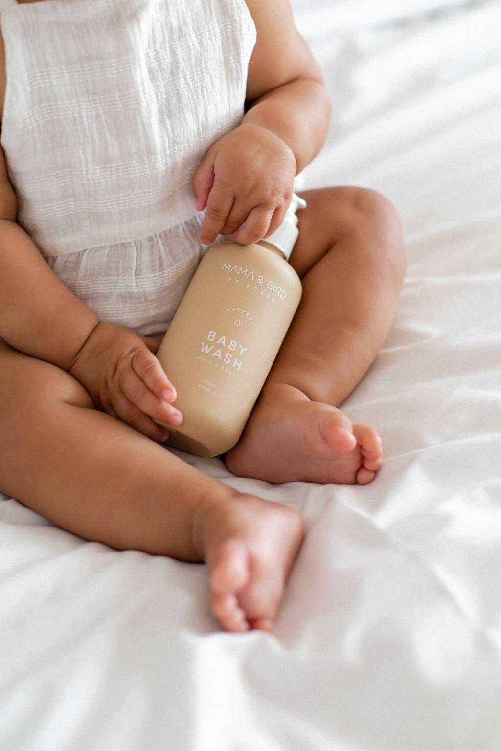 A baby holding a Mama and Bird baby wash bottle.