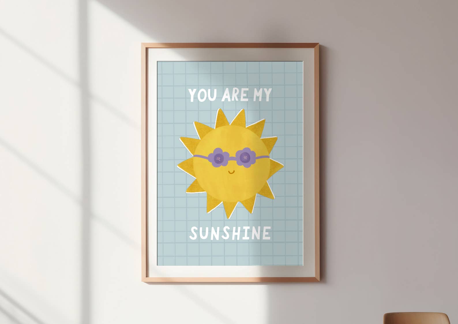 An art print with a picture of a sun wearing purple flower shaped sunglasses with the words "you are my" above it and the word "sunshine" below it. The print is on a blue background with a square pattern over the top. The art print is by Lauren Sissons Studio.