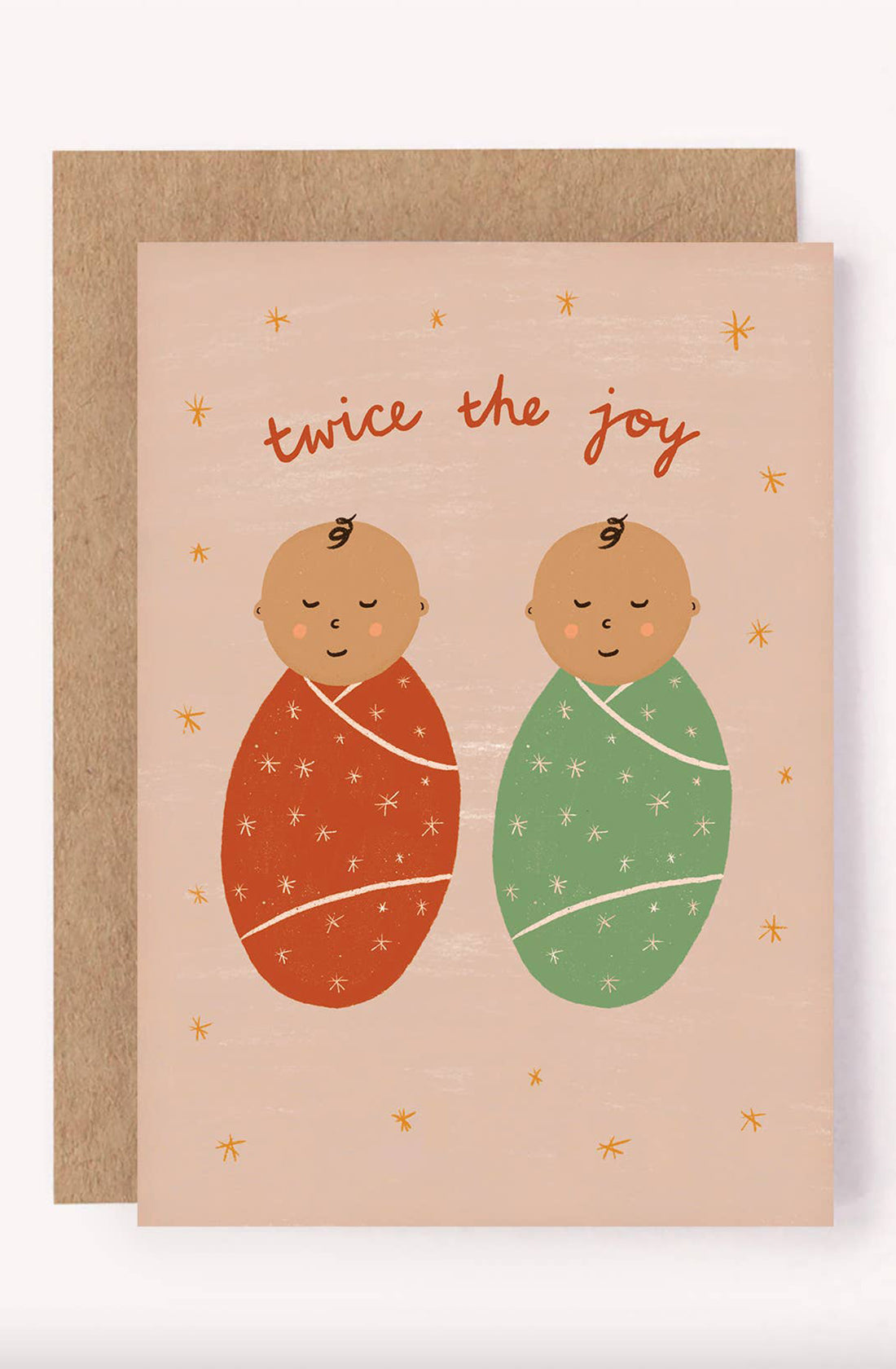 Presenting the New Baby Greeting Card "Twice The Joy" by LAUREN SISSONS STUDIO, featuring two charming illustrated swaddled babies—one in a red blanket and the other in green. Adorned with playful text that reads "twice the joy" accompanied by star-like decorations, this card is printed on recycled paper and comes with a brown envelope peeking out from behind.