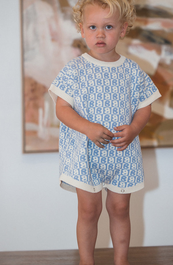 Blonde toddler wearing the BB romper in blue with a neutral coloured painting in the background