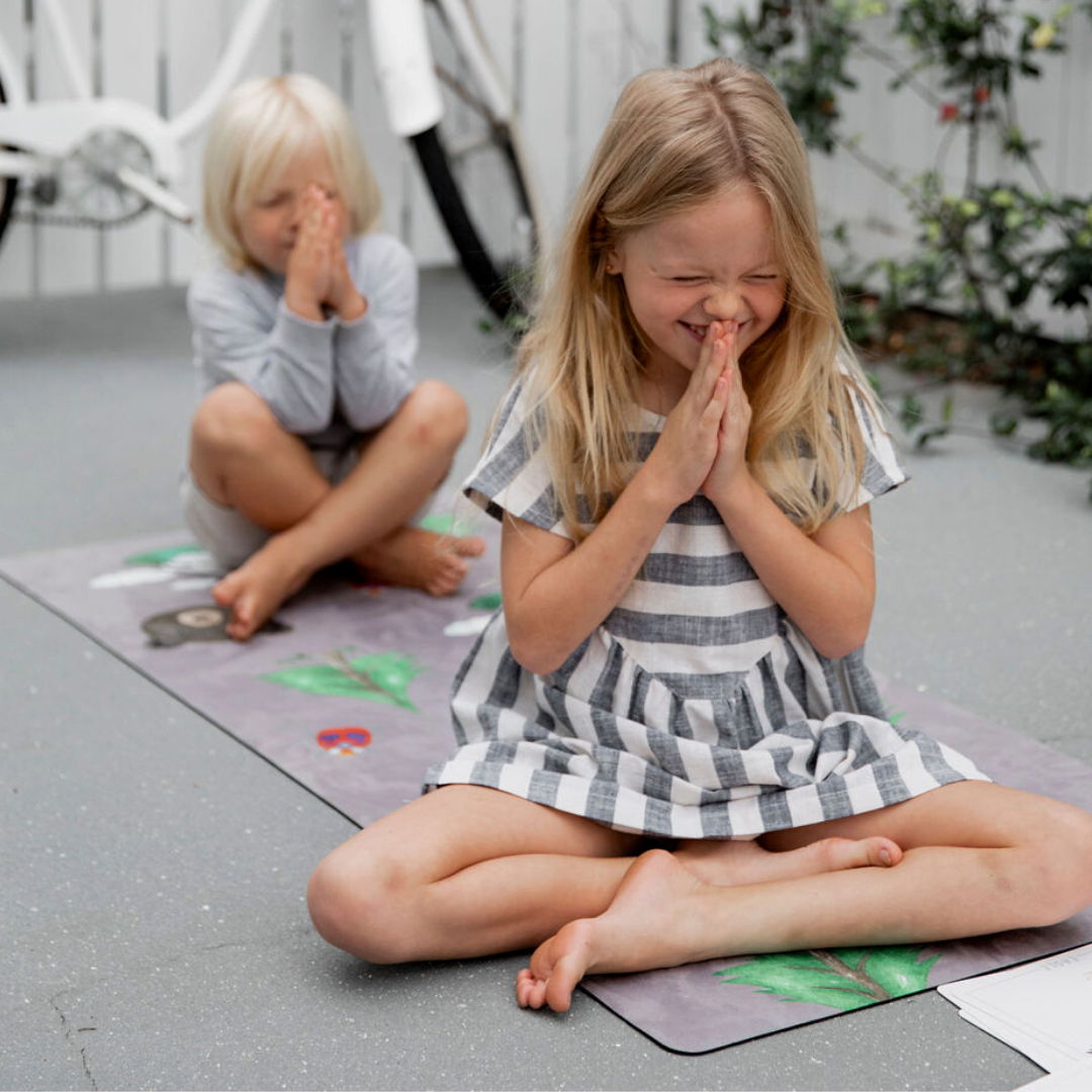 Two kids sitting on the nature kids yoga mat in a meditation pose.