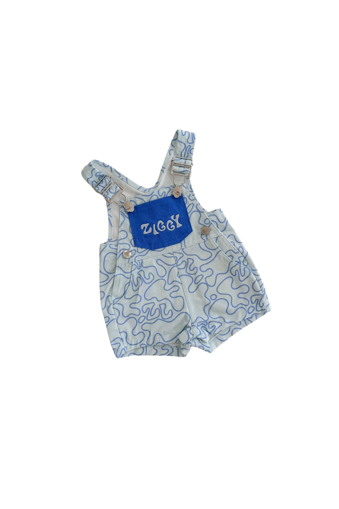 The "Short Overalls Zen" by ZIGGY LOU are children's shortalls made from 100% cotton canvas and feature a playful blue and white squiggly line pattern. A stylish blue pocket on the chest displays "Ziggy" in white writing. They have adjustable straps with buttons and are displayed flat against a black background.