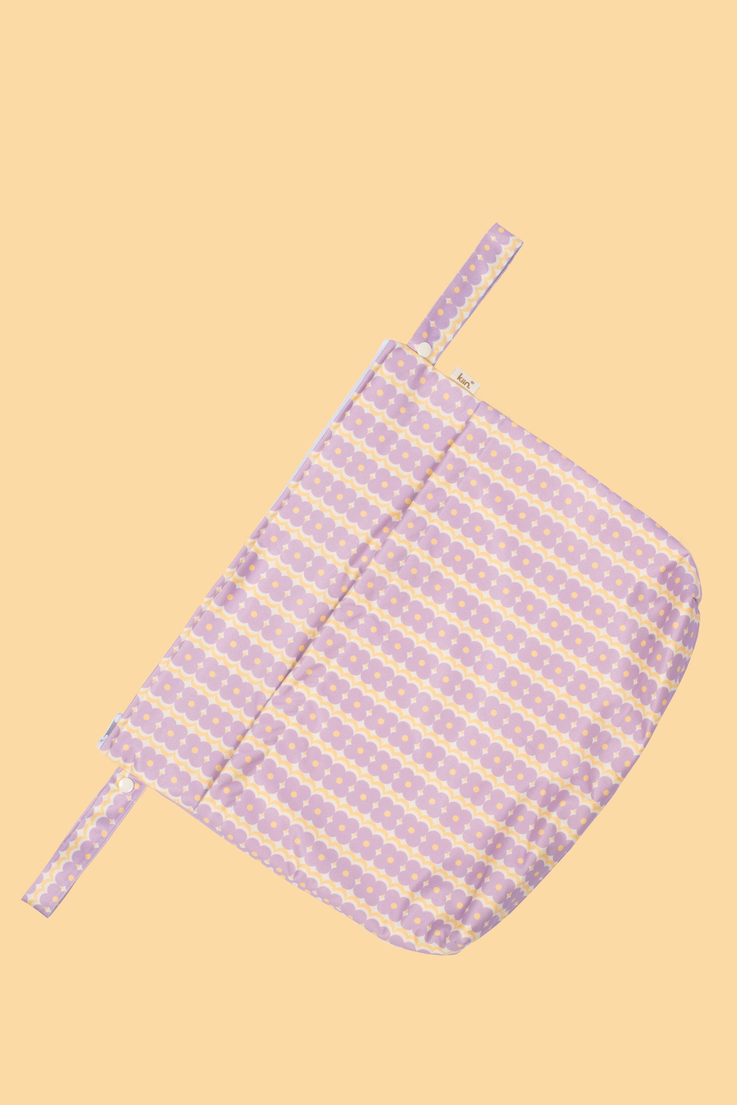 The folded Reusable Wet Bag Flower Power by KIIN BABY in a pink and yellow striped fabric with dots gracefully rests against a peach background. Two visible straps enhance its eco-friendly charm, making it perfect for reusable wet bags.