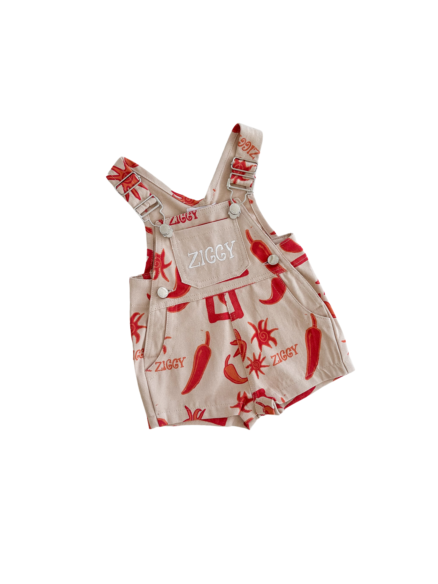 Beige shortalls for children by ZIGGY LOU, featuring chili pepper and sun designs and called "Ziggy Lou ~ Short Overalls Chilli." They have adjustable buttoned shoulder straps, a front pocket, and a black background.