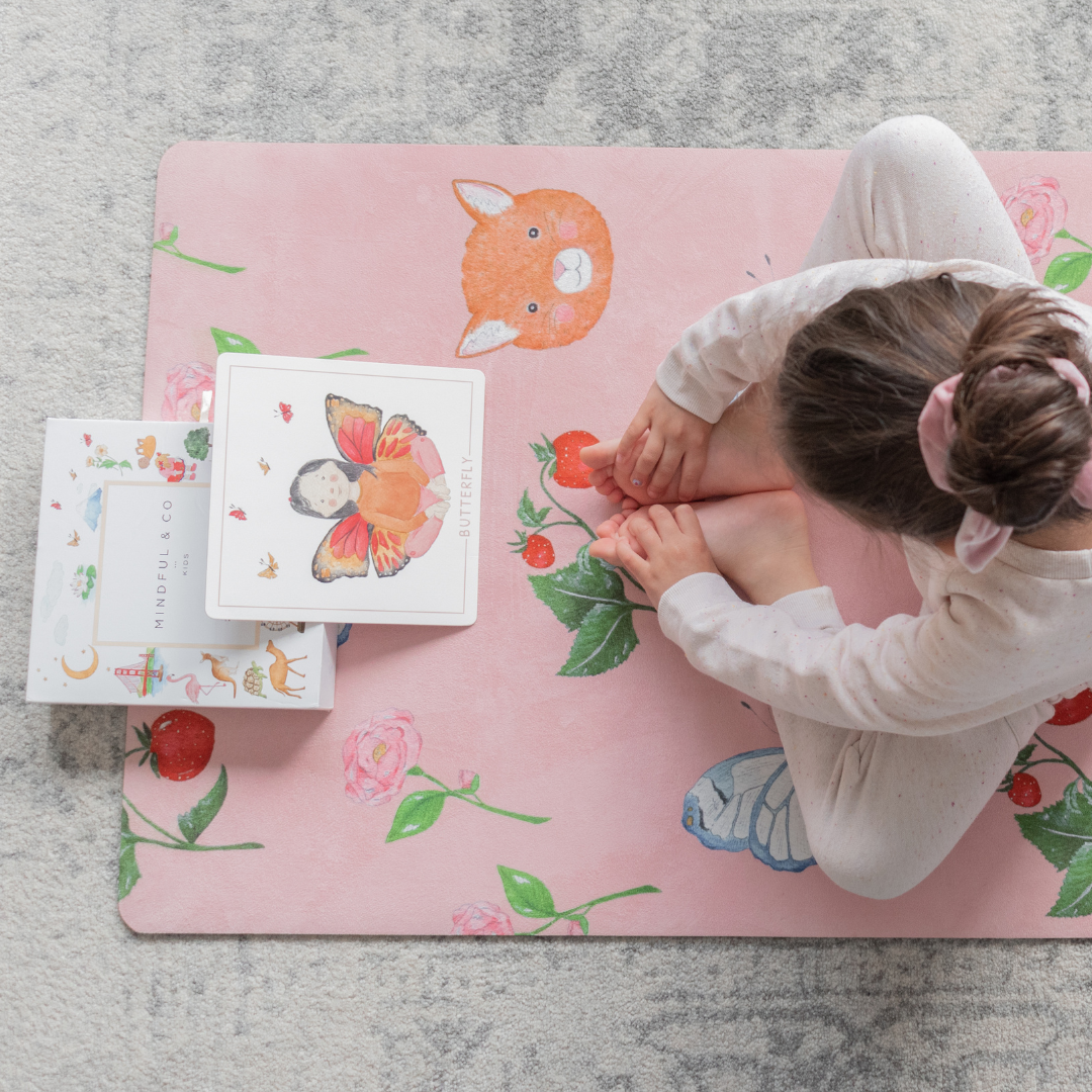 A young girl sitting on the sweet themed pink kids yoga mat in a meditation pose.