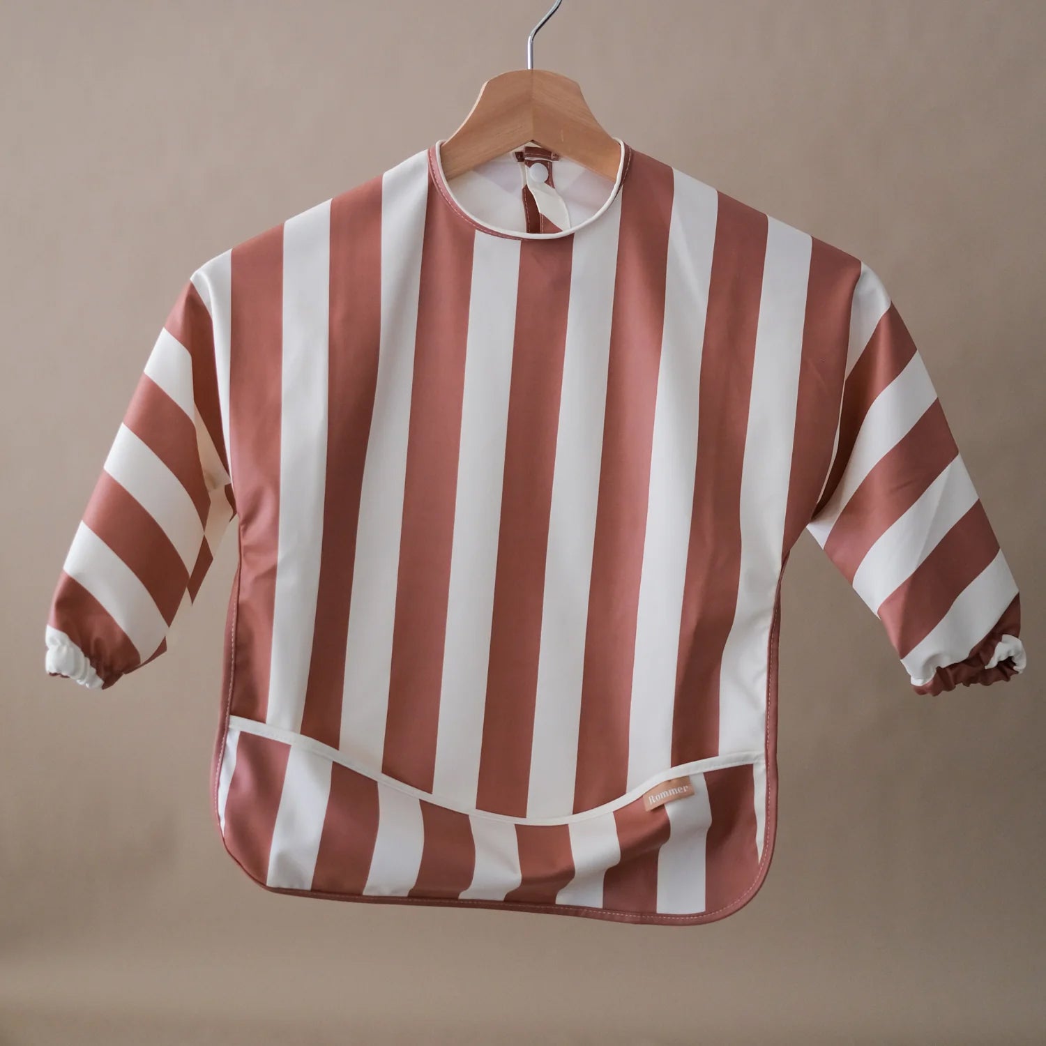 ROMMER Smock Bib in Cinnamon Stripe hanging from a coat hanger.