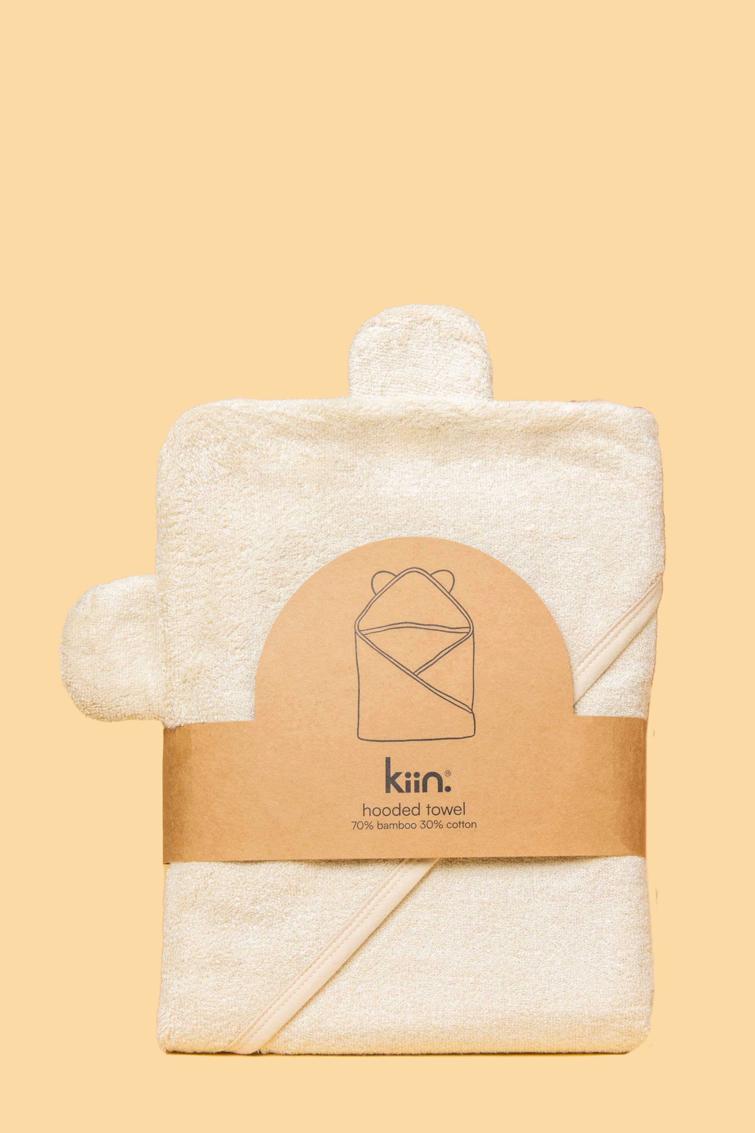 A neatly folded ivory hooded towel by KIIN BABY, crafted from 70% hypoallergenic bamboo fabric and 30% cotton, features a minimalistic design and a brown paper label with the brand name and a graphic of the towel.