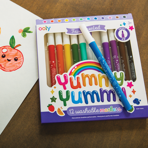 A packet of OOLY fruity scented washable markers next to a drawing of an apple with the colour blue marker sitting on top of the packet.