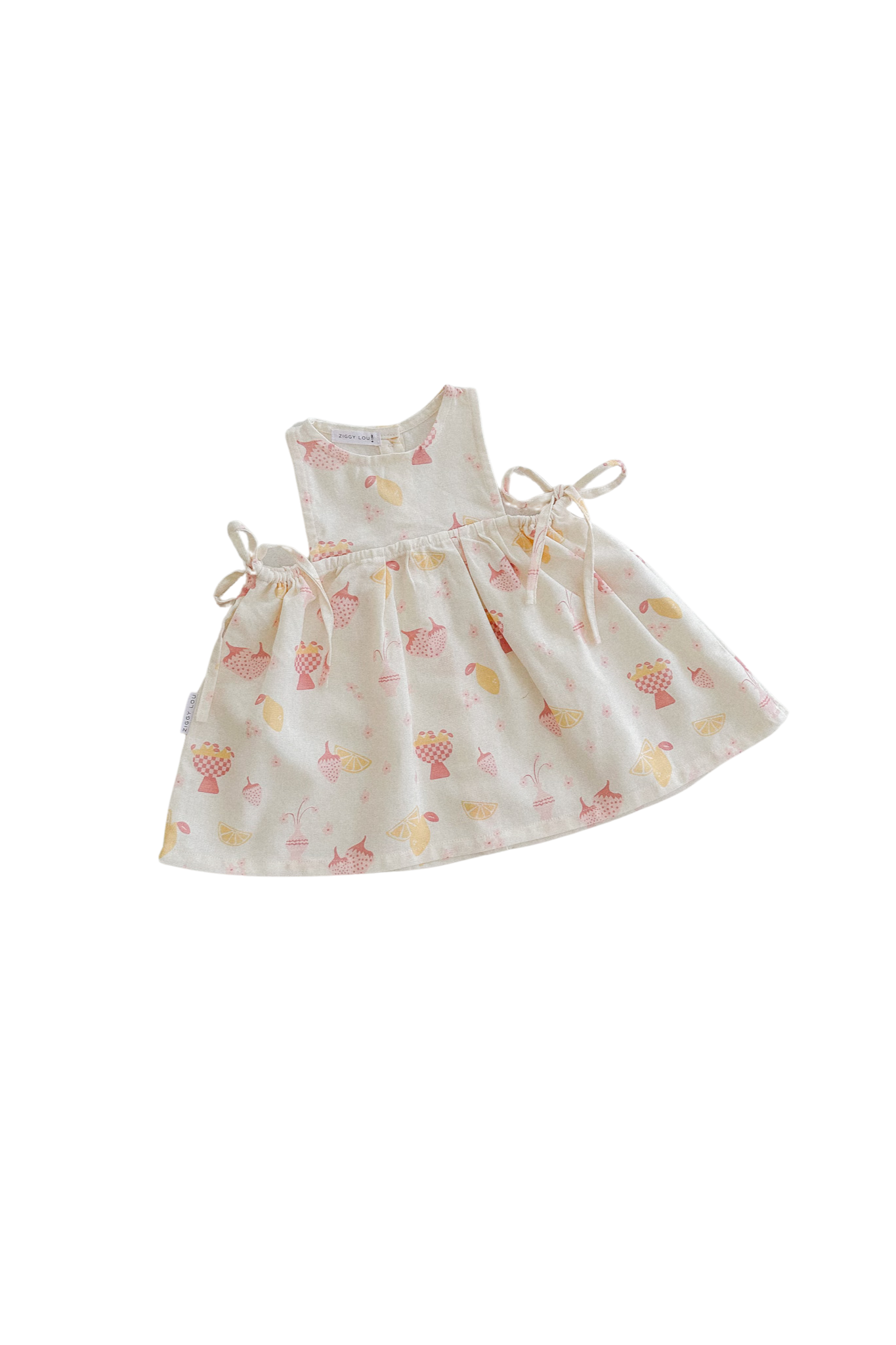 The Sofia Dress August by ZIGGY LOU is a white baby dress featuring the vibrant August print, which includes colorful patterns of cupcakes, ice cream cones, and various treats. This design has small bows on the sides set against a black background and is crafted from an ethically made linen blend for both comfort and style.