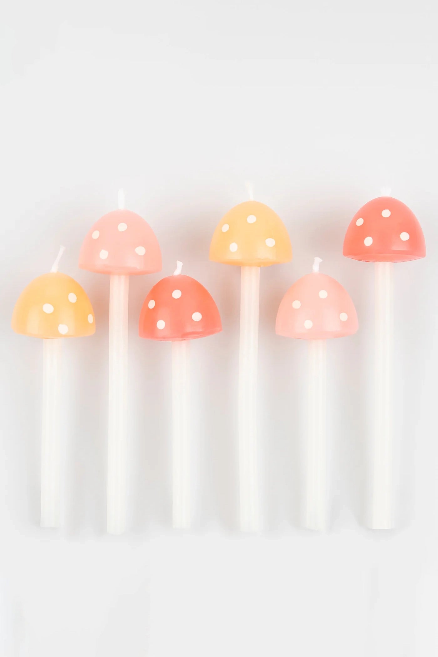 A set of six MERI MERI Mushroom Birthday Candles, featuring a tall white design with pastel tops in shades of pink, peach, and coral, each decorated with charming white polka dots. These delightful candles are ideal for bringing a whimsical touch to your garden party, especially when displayed against a simple white backdrop.