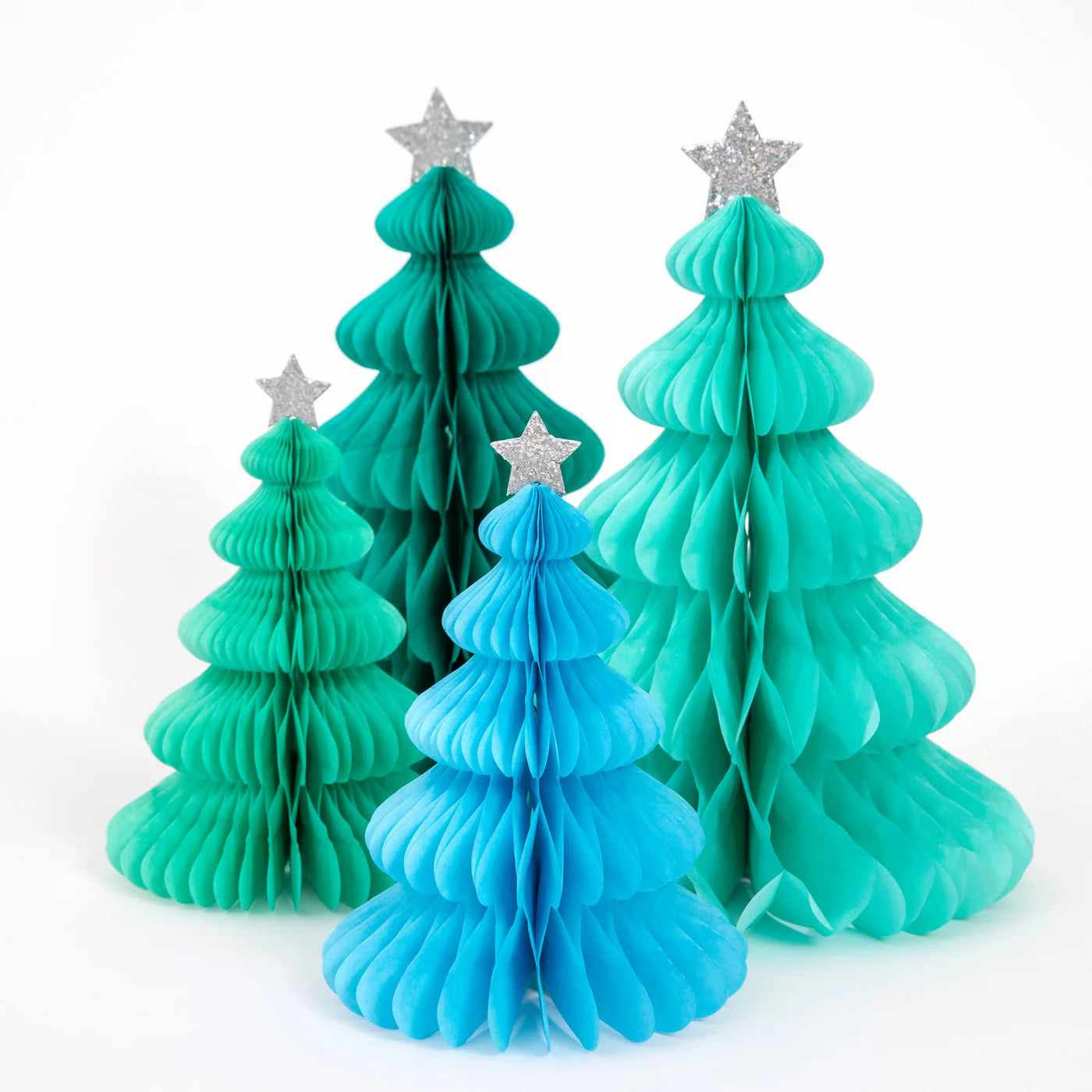 Against a white background, four paper Christmas trees from the MERI MERI Rainbow Forest Honeycomb Decorations collection, in shades of teal and blue, are displayed. Each tree features a silver star adorned with plant-based glitter and exhibits a layered accordion-style design.