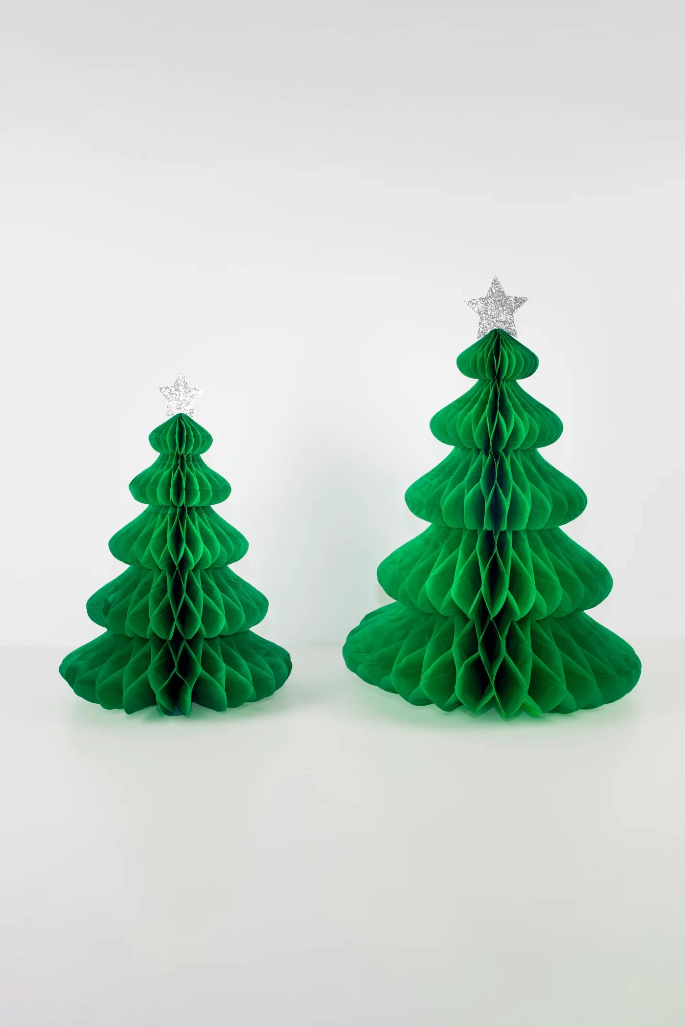 Two elegant Giant Honeycomb Trees from MERI MERI are arranged side by side against a plain white backdrop. Each Christmas decoration is adorned with a glittery star, adding a touch of sparkle. The tree on the right is slightly larger than its companion, creating a charming holiday display.