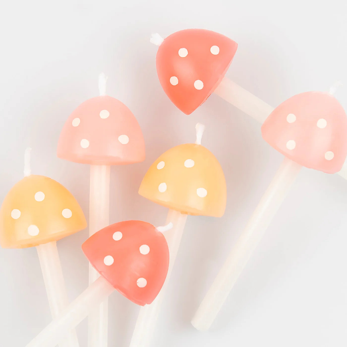 The MERI MERI Mushroom Birthday Candles, available in a delightful pack of 6 in two different sizes, feature whimsical mushroom shapes with white stems and caps in pastel shades of pink, red, and orange adorned with charming white polka dots. Laid out on a light background, they are perfect for adding enchanting charm to your next garden party.