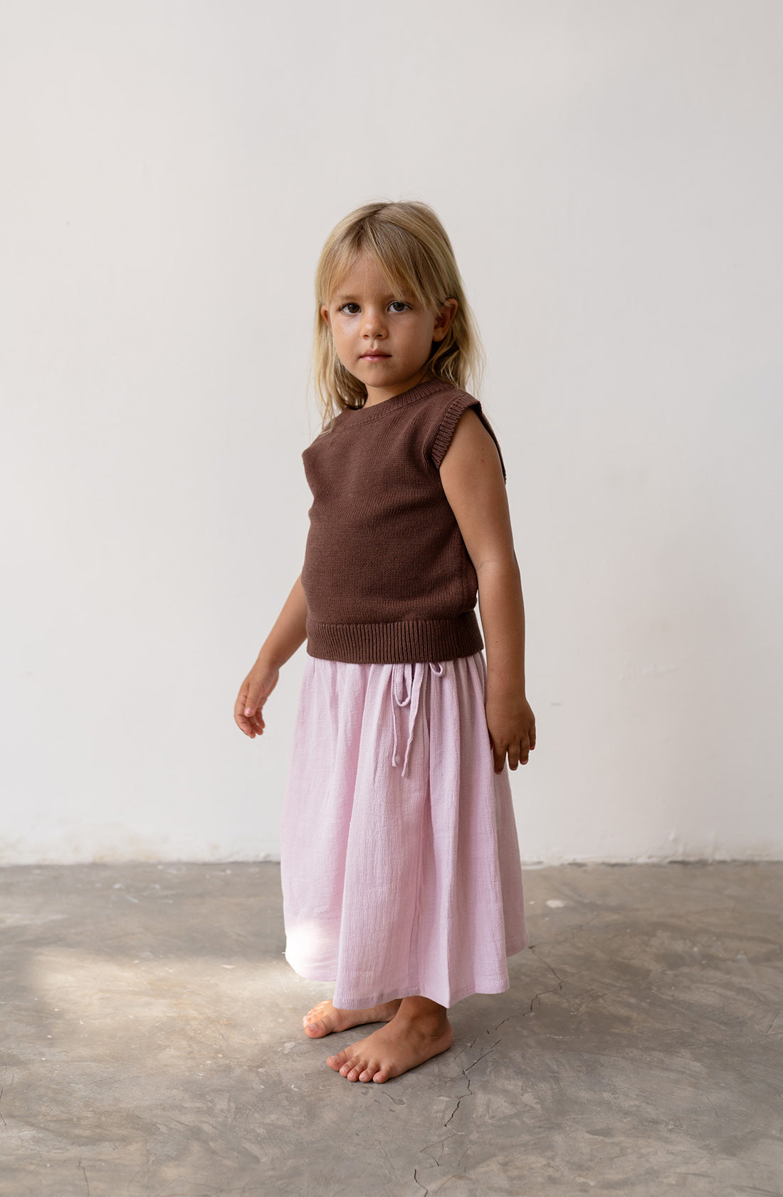 Young girl wearing knit vest in cocoa with a pink skirt.