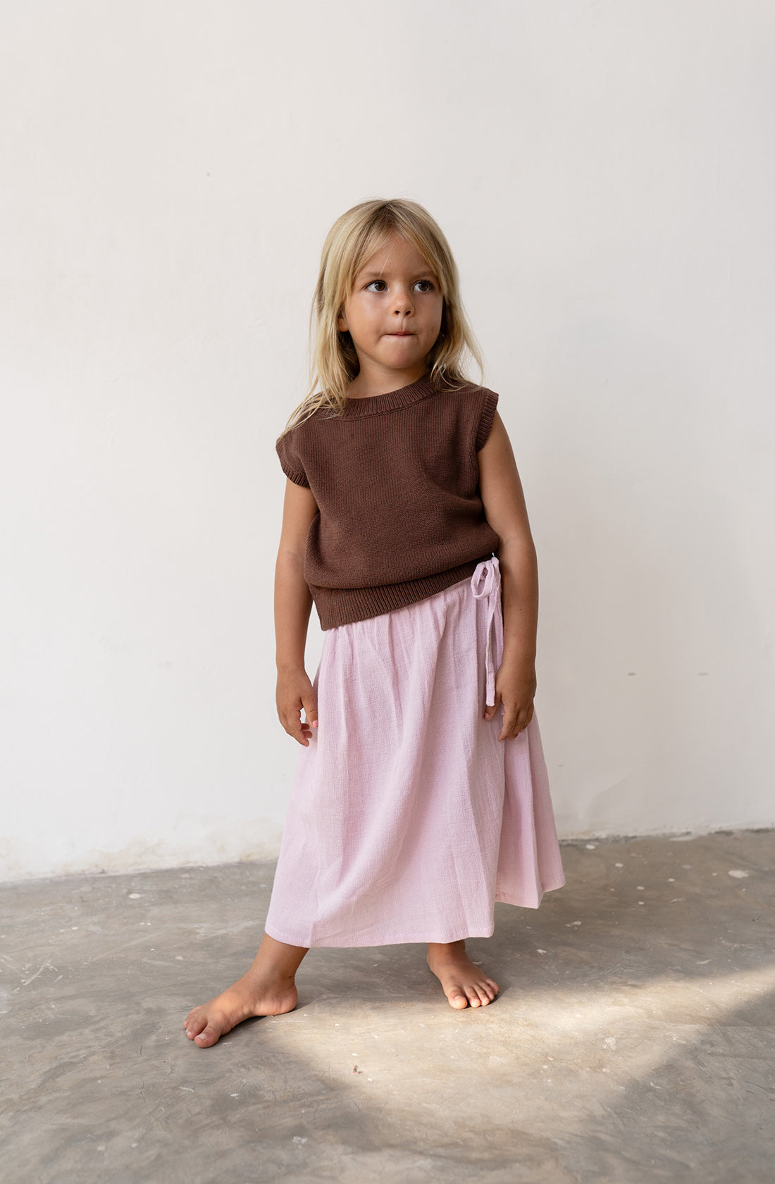 Young girl wearing the knit vest in cocoa and a pink skirt.