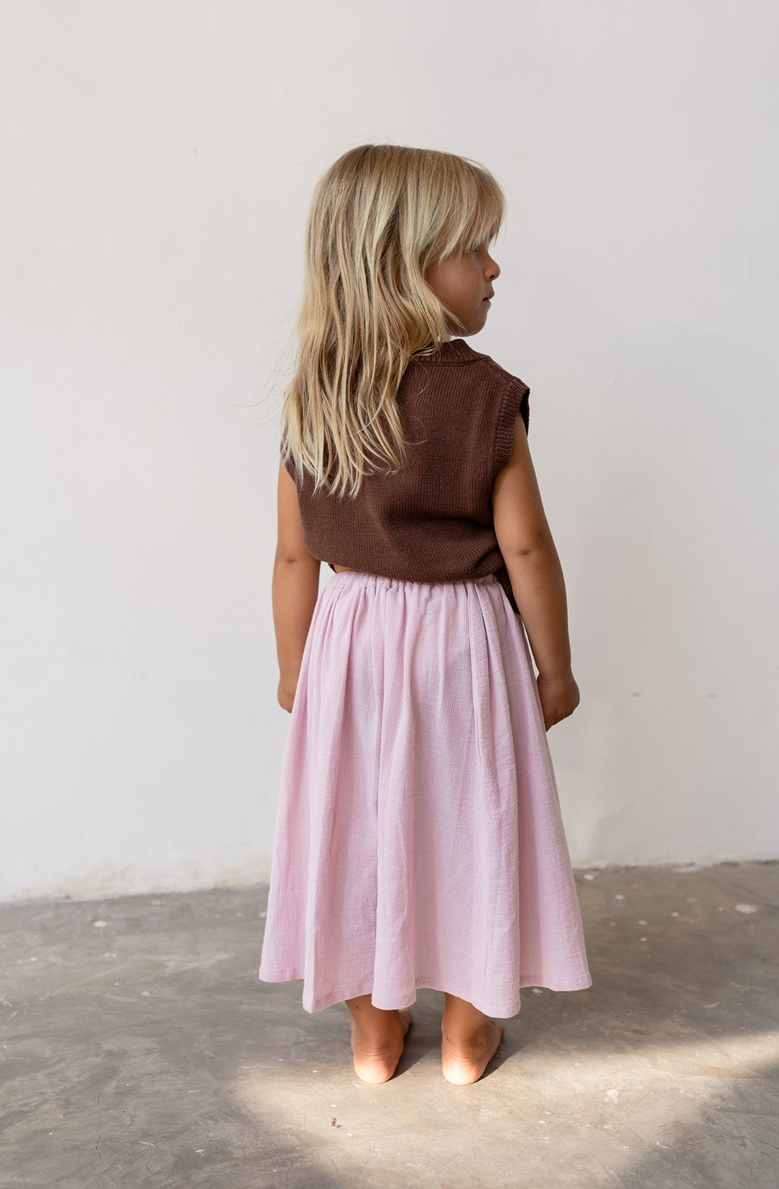 Young girl wearing the knit vest in cocoa and a pink skirt,