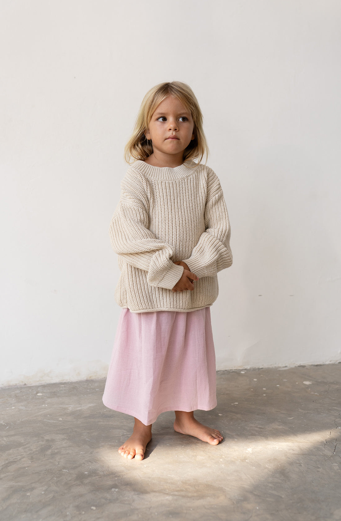 Little girl wearing the chunky knit jumper in natural with a pink skirt.