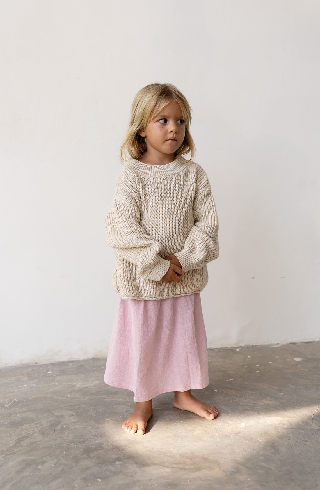 A young girl wearing the Chunky knit jumper in natural with a pink skirt.