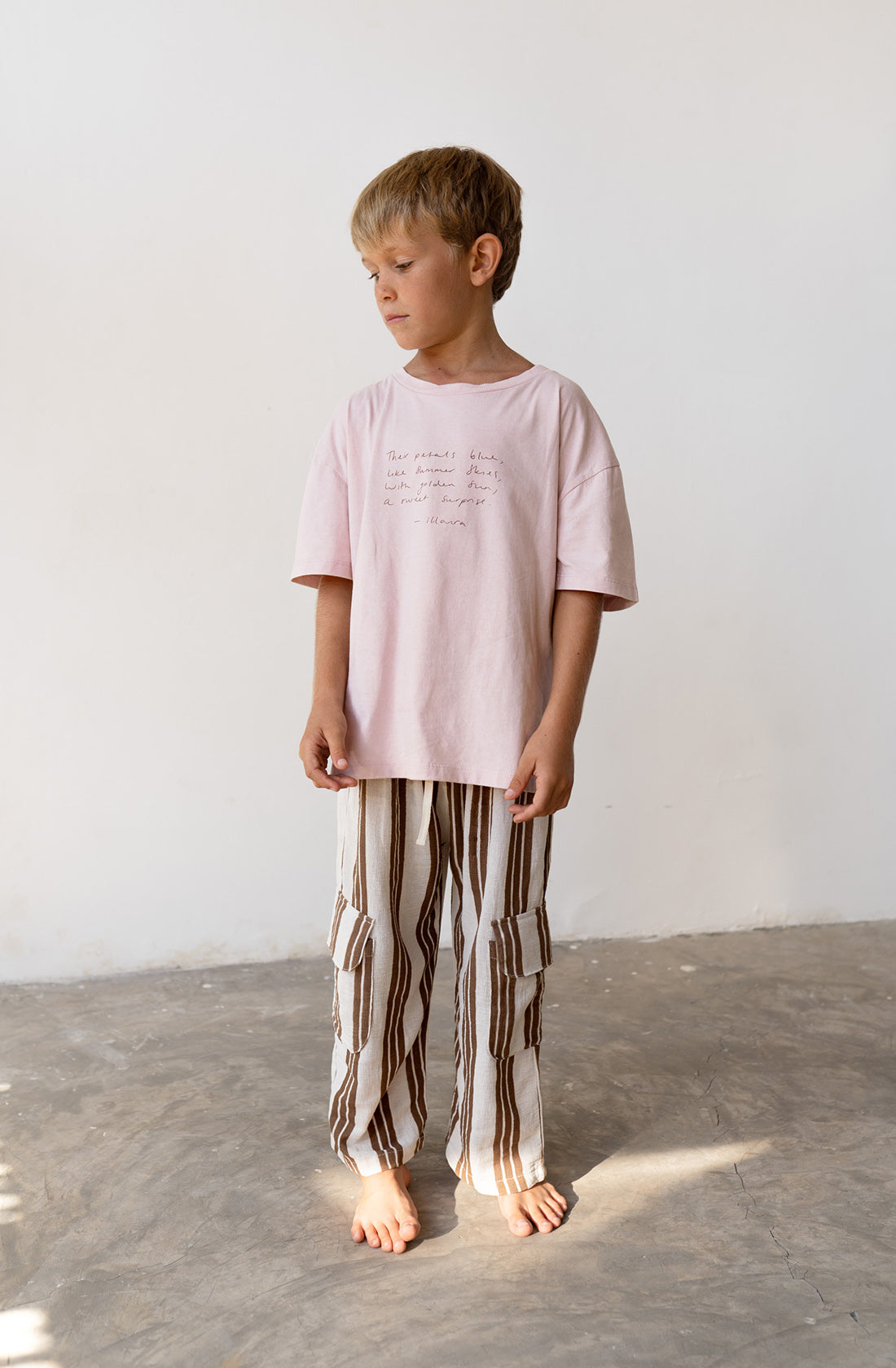 Young boy wearing the henna pants in cocoa stripe with a pink t shirt.