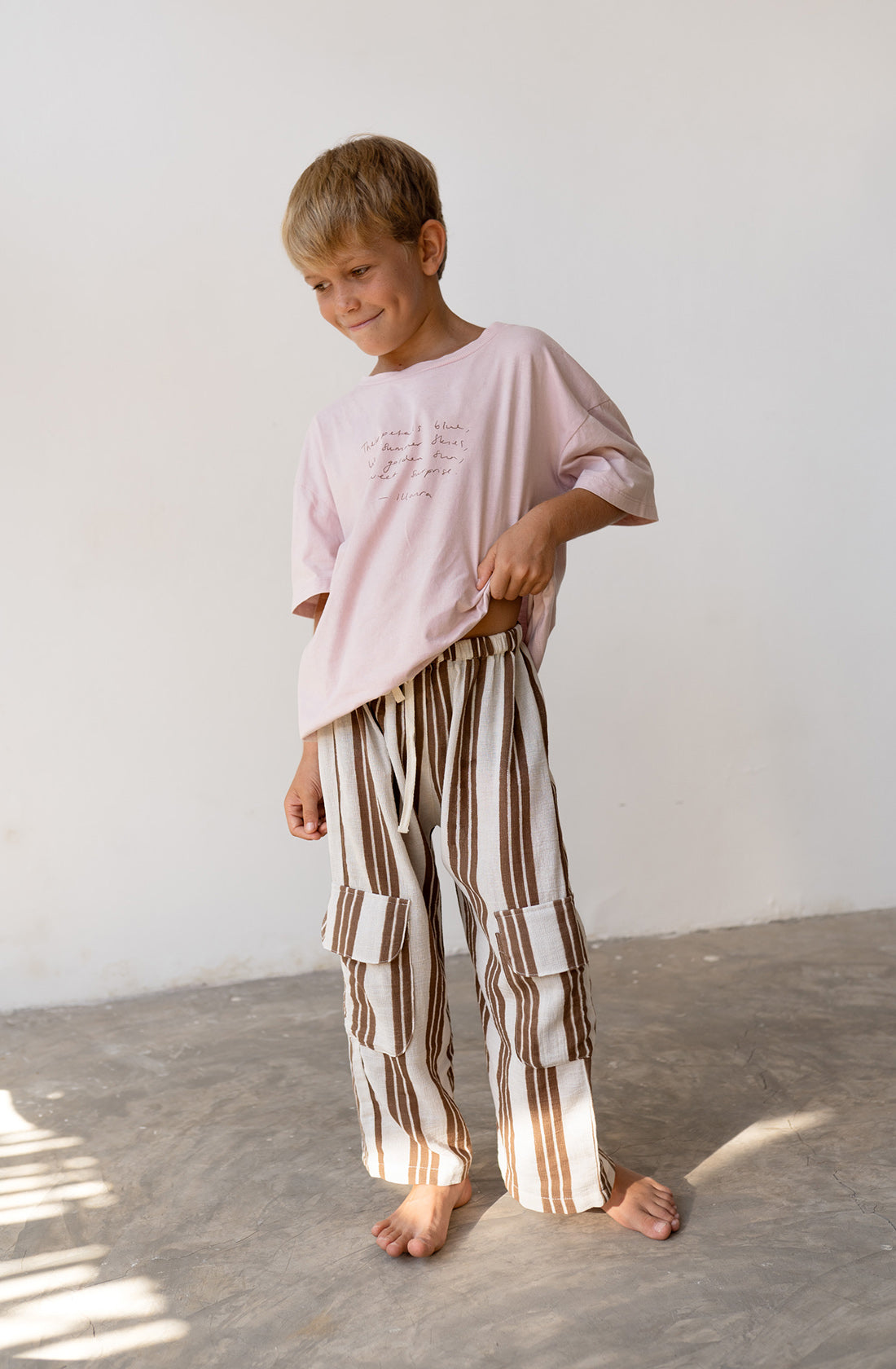 Young boy wearing the henna pants in cocoa stripe with a pink t shirt.