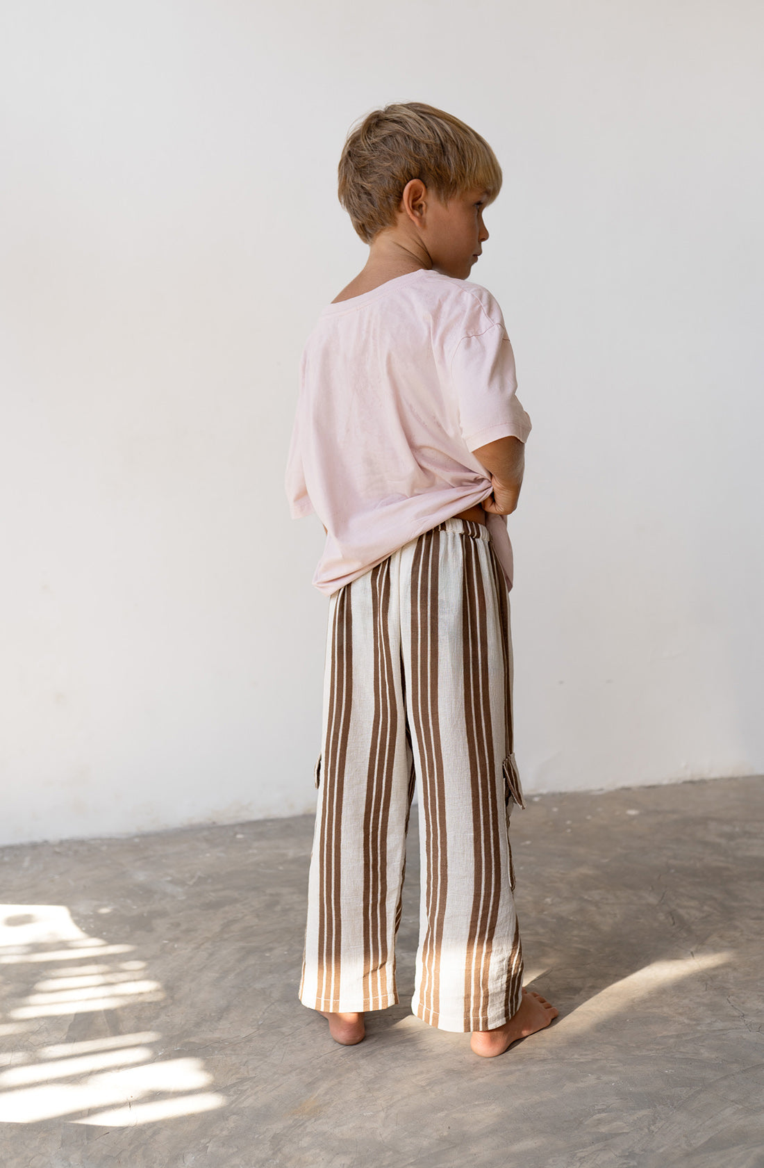 Young boy wearing the henna pants in cocoa stripe with a pink shirt.