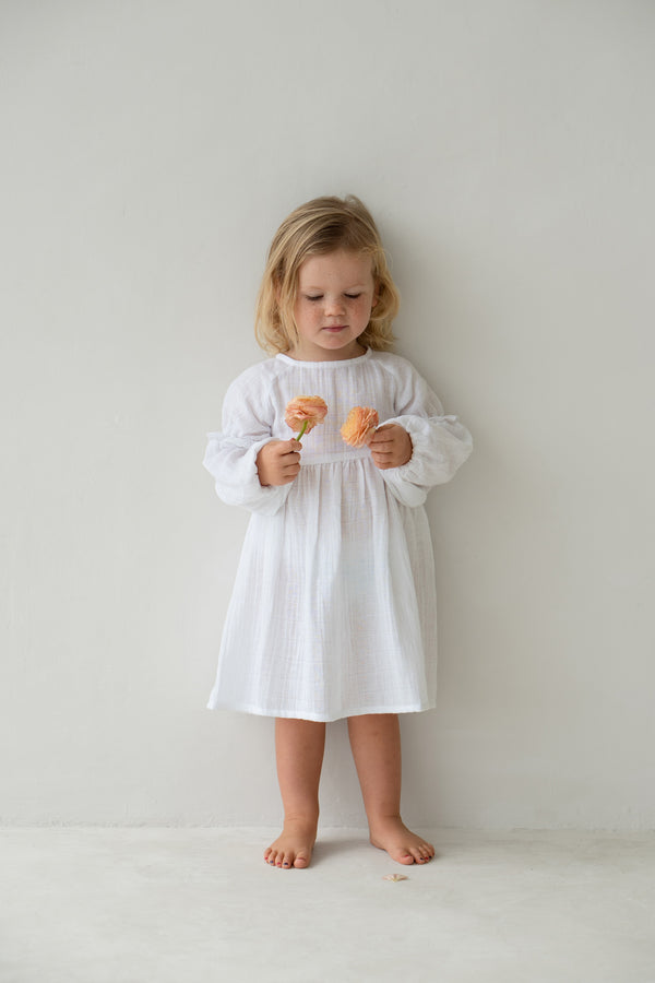 Blonde toddler girl holding two flowers and wearing white Maggie dress