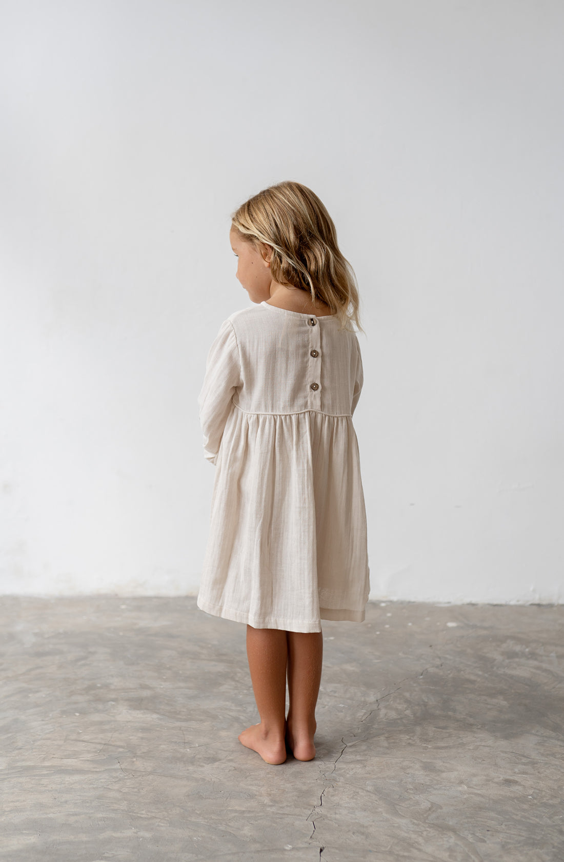 Young girl wearing the yumi dress in natural from the back.