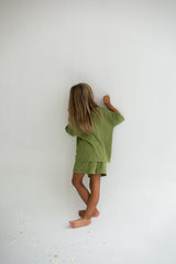 Girl turned to face a wall while wearing the olive tee and short set